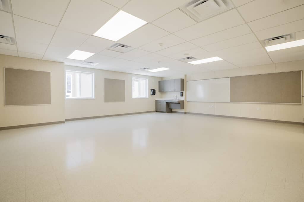 An empty classroom interior with a sink and cabinets in the far right corner.
