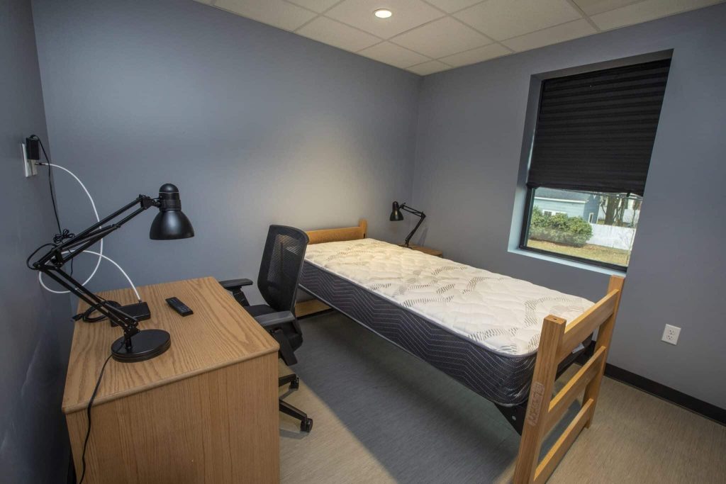 A modern bedroom setup in a triumph modular building featuring a simple desk, chair, and an unmade bed, showcasing the functionality of modular construction for both permanent and temporary modular buildings.